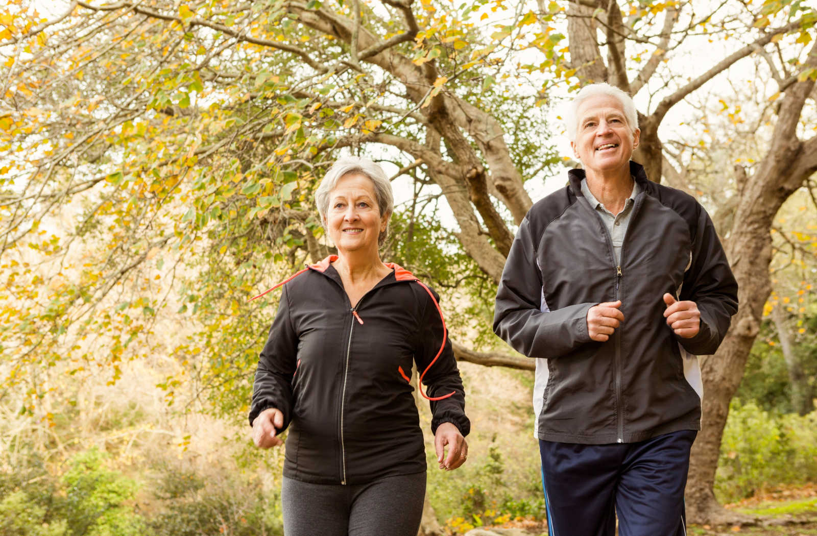 A senior woman and a senior man smiling while walking in a park.