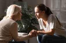 A mother and her daughter talking to each other while sitting on a couch.