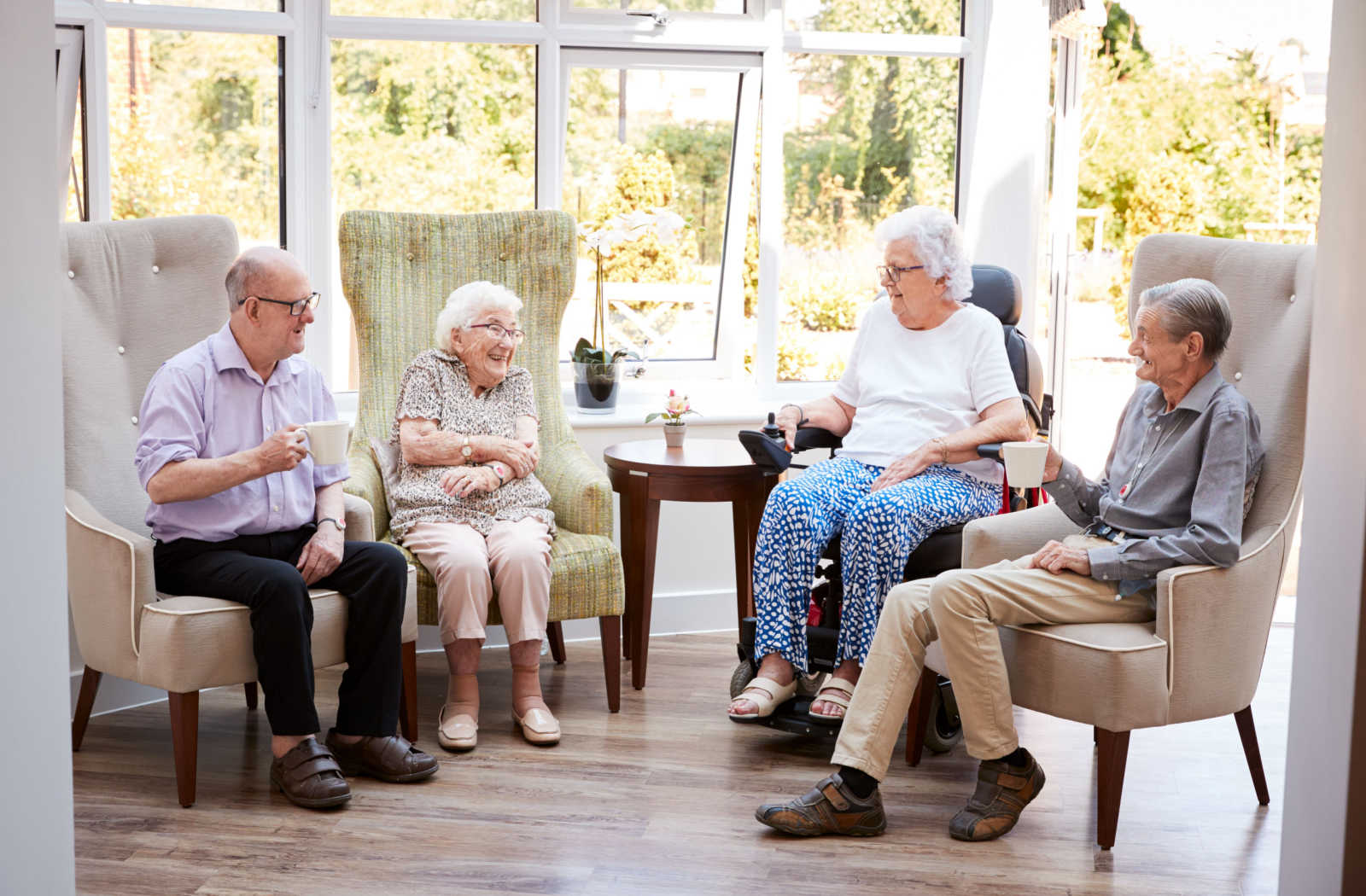 Group of seniors sitting smiling and chatting with each other in a senior living facility.