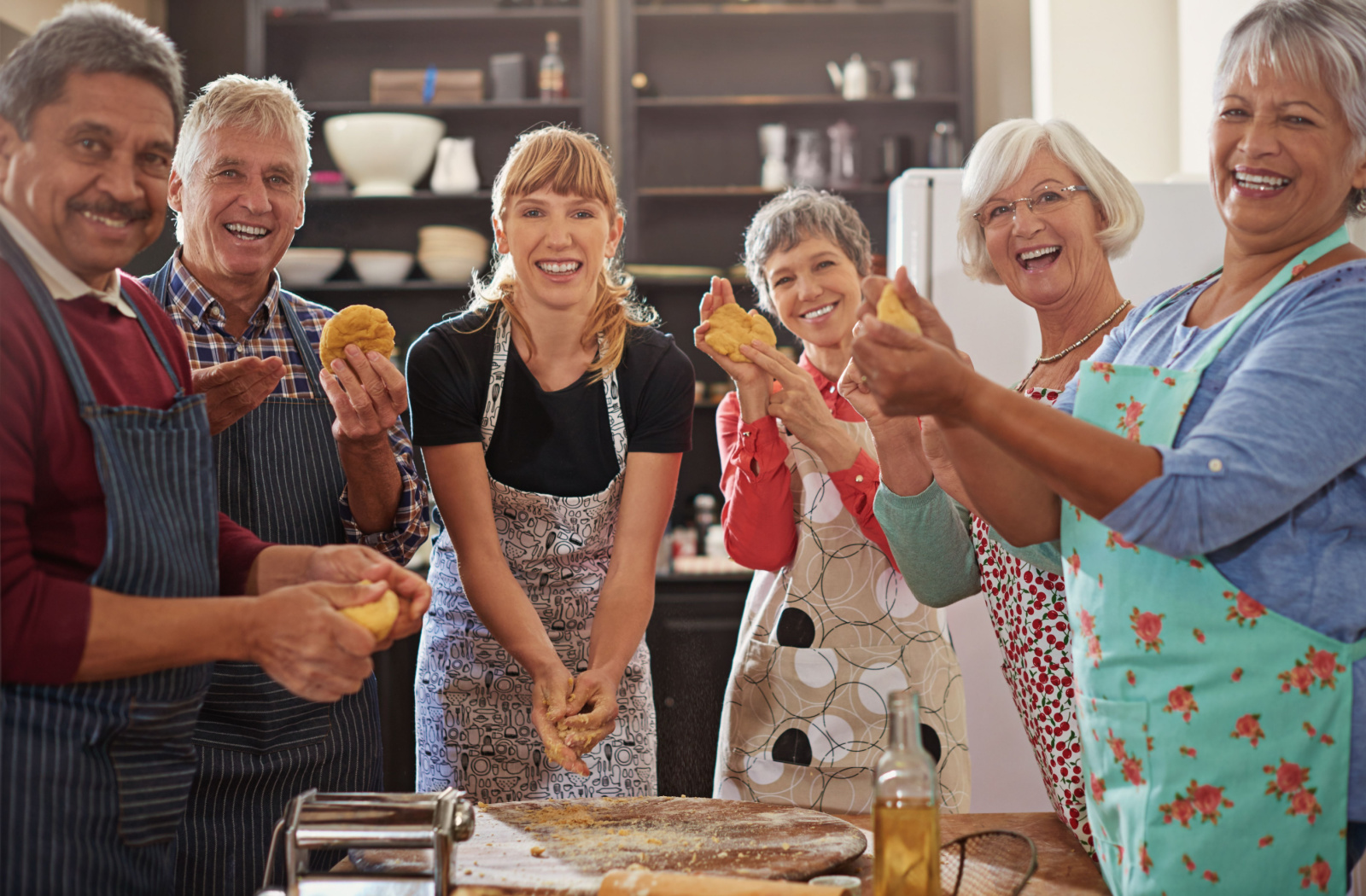 A group of seniors in a baking class with their instructor, each holding dough, smiling and looking directly at the camera