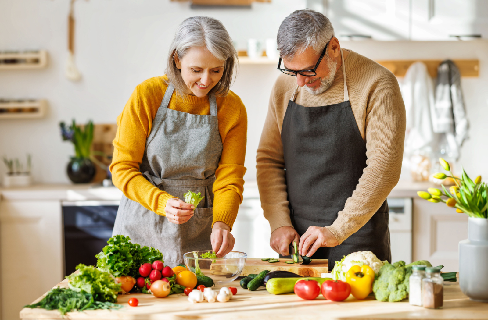 A senior man and a senior woman preparing a bowl of salad in the kitchen.