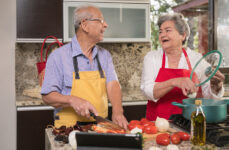 An elderly couple happily cooking a healthy meal together.