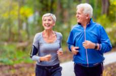 A senior man and a woman smiling while jogging outdoors