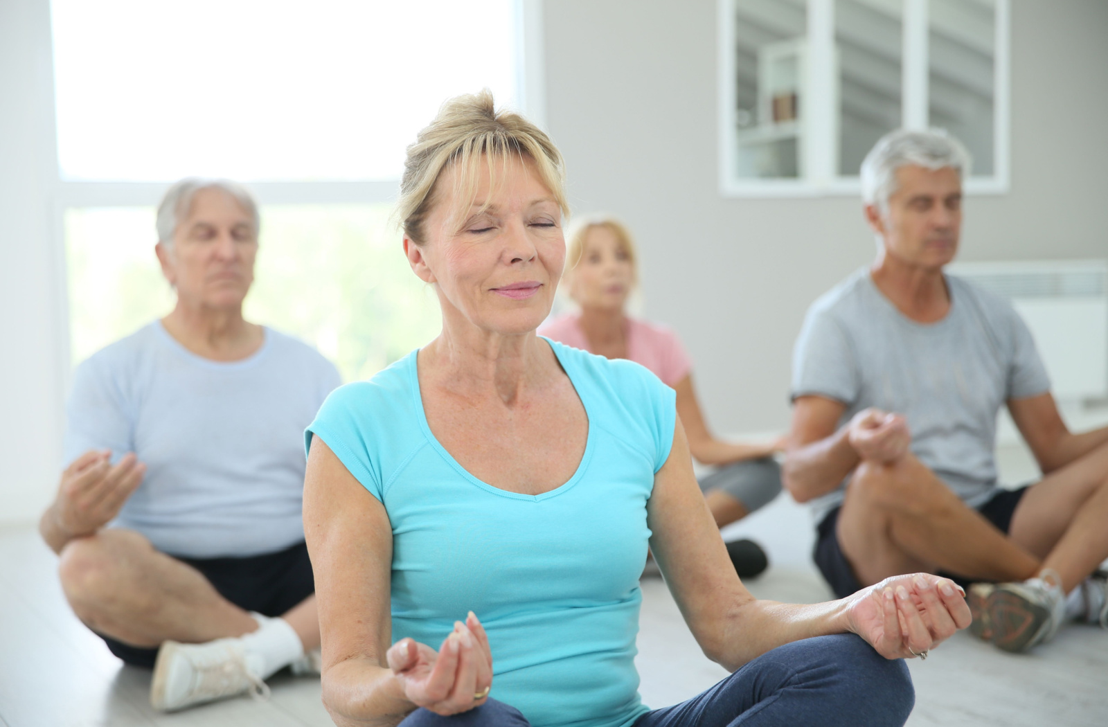 A group of seniors with closed eyes practicing yoga and are sitting on yoga mats