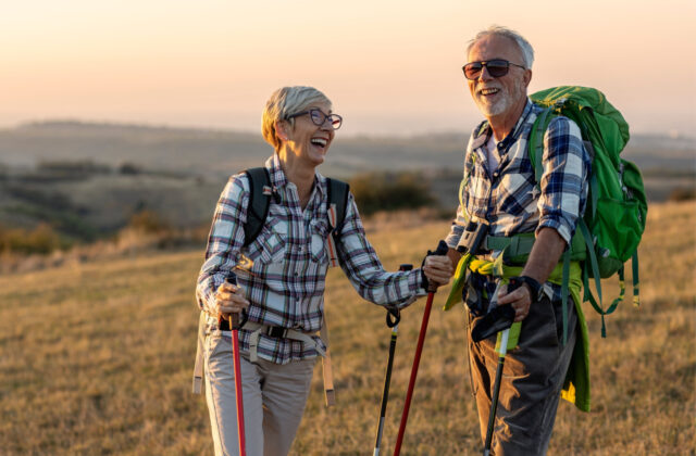 An older man and woman smiling and enjoying a sunset hike together